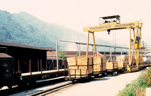 Un train de planches en court de transbordement sous le portique de la gare de Kapfenberg en 1976